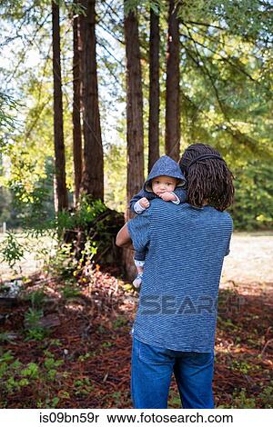 Stock Photography - Mature man carrying baby son in forest, portrait. Fotosearch