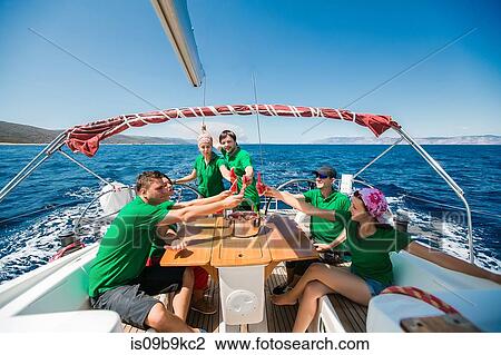 Stock Image - Men and young women on board yacht raising a toast with sliced water melon, Croatia. Fotosearch