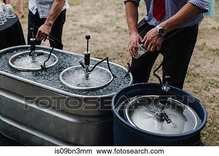 Men pouring beer from keg in cooling bath at barbecue, cropped View Large Photo Image Picture - Men pouring beer from keg in cooling bath at barbecue, cropped. Fotosearch