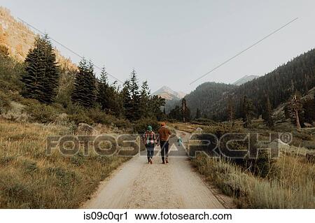 Stock Image - Mid adult couple following toddler daughter walking on rural valley road, rear view, Mineral King, California, USA. Fotosearch