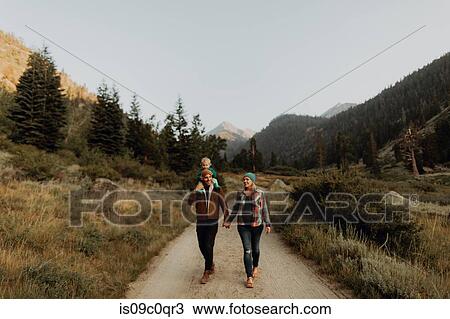 Stock Image - Mid adult couple giving toddler daughter a shoulder carry on rural valley road, Mineral King, California, USA. Fotosearch
