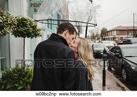 Stock Photography - Mid adult couple in street, kissing, holding umbrella. Fotosearch