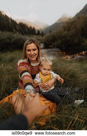 Stock Photo - Mid adult couple sitting with toddler daughter holding hands by rural river, Mineral King, California, USA. Fotosearch
