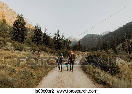 Stock Image - Mid adult couple walking with toddler daughter on rural valley road, Mineral King, California, USA. Fotosearch