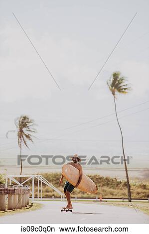 Mid adult male skateboarder carrying surfboard, skateboarding on coastal road, Haiku, Hawaii, USA View Large Photo Image Picture - Mid adult male skateboarder carrying surfboard, skateboarding on coastal road, Haiku, Hawaii, USA. Fotosearch