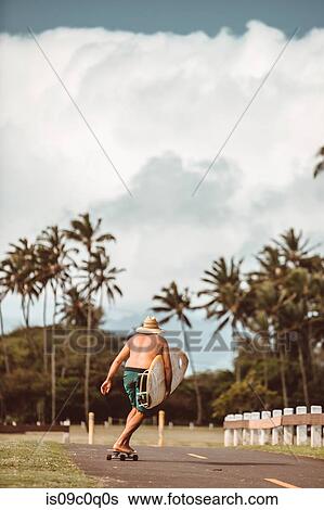 Mid adult male skateboarder carrying surfboard, skateboarding on rural road, rear view, Haiku, Hawaii, USA View Large Photo Image Stock Photograph - Mid adult male skateboarder carrying surfboard, skateboarding on rural road, rear view, Haiku, Hawaii, USA. Fotosearch