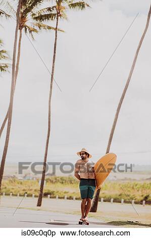 Mid adult male skateboarder carrying surfboard, standing on skateboard on coastal road, Haiku, Hawaii, USA View Large Photo Image Stock Photography - Mid adult male skateboarder carrying surfboard, standing on skateboard on coastal road, Haiku, Hawaii, USA. Fotosearch