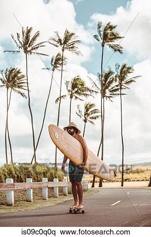 Mid adult male skateboarder carrying surfboard, skateboarding on coastal road, Haiku, Hawaii, USA View Large Photo Image Stock Photography - Mid adult male skateboarder carrying surfboard, skateboarding on coastal road, Haiku, Hawaii, USA. Fotosearch