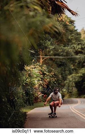Mid adult male skateboarder crouching while skateboarding along rural road, Haiku, Hawaii, USA View Large Photo Image Stock Image - Mid adult male skateboarder crouching while skateboarding along rural road, Haiku, Hawaii, USA. Fotosearch