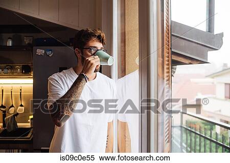 Mid adult man drinking coffee while looking out through apartment window View Large Photo Image Stock Photography - Mid adult man drinking coffee while looking out through apartment window. Fotosearch