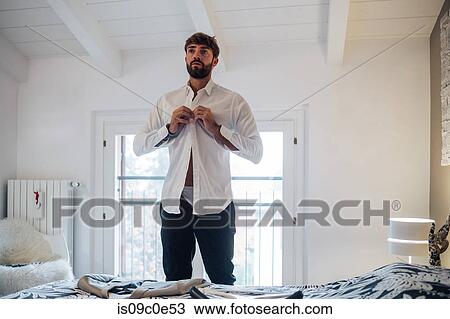 Mid adult man fastening shirt in bedroom View Large Photo Image Stock Image - Mid adult man fastening shirt in bedroom. Fotosearch