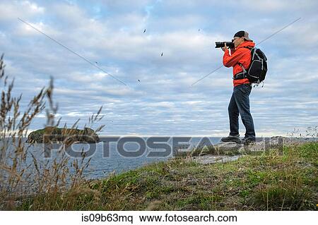 Stock Photography - Mid adult man photographing coastline, Saint John, Canada,. Fotosearch