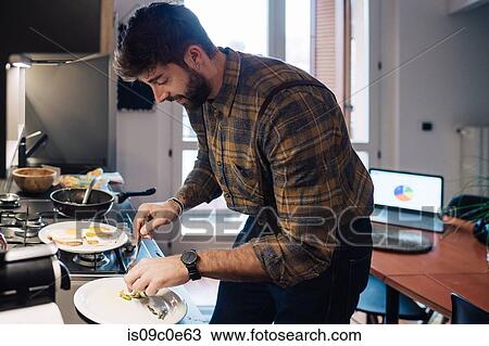 Stock Image - Mid adult man plating food at kitchen counter. Fotosearch