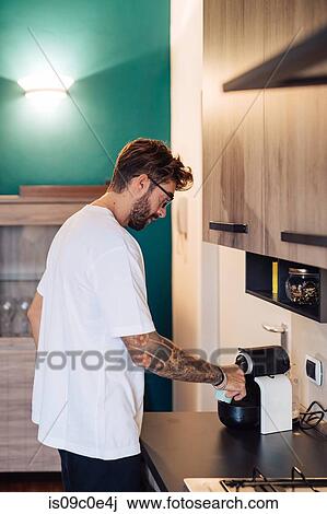 Stock Image - Mid adult man pouring coffee from coffee machine on kitchen counter. Fotosearch