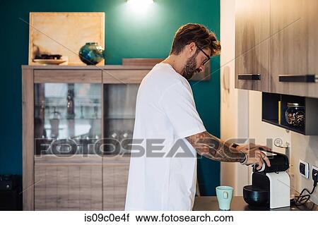 Stock Image - Mid adult man preparing coffee machine on kitchen counter. Fotosearch