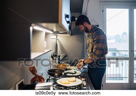 Stock Photo - Mid adult man preparing food at kitchen hob. Fotosearch