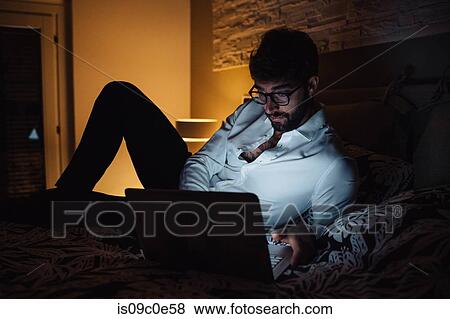 Mid adult man reclining on bed using laptop at night View Large Photo Image Stock Photo - Mid adult man reclining on bed using laptop at night. Fotosearch