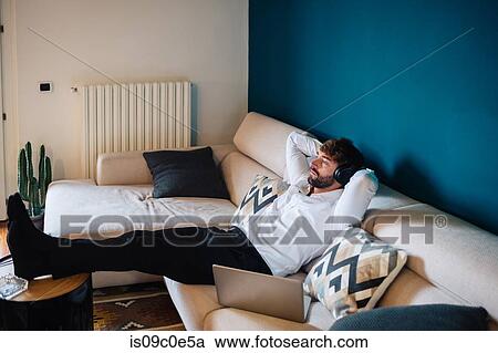 Mid adult man reclining on sofa listening to headphones View Large Photo Image Stock Image - Mid adult man reclining on sofa listening to headphones. Fotosearch