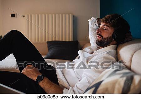 Mid adult man reclining on sofa listening to headphones with eyes closed View Large Photo Image Stock Image - Mid adult man reclining on sofa listening to headphones with eyes closed. Fotosearch