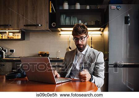 Mid adult man sitting at kitchen table with laptop and credit card View Large Photo Image Stock Image - Mid adult man sitting at kitchen table with laptop and credit card. Fotosearch