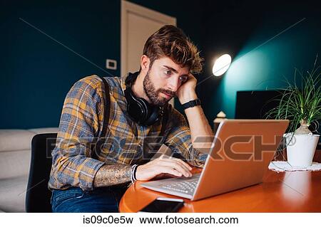 Mid adult man sitting at living room table looking at laptop View Large Photo Image Stock Photo - Mid adult man sitting at living room table looking at laptop. Fotosearch