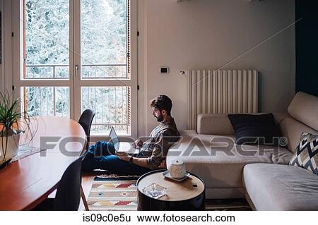 Mid adult man sitting on living room floor using laptop View Large Photo Image Stock Photograph - Mid adult man sitting on living room floor using laptop. Fotosearch