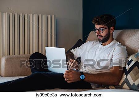 Mid adult man sitting on sofa typing on laptop View Large Photo Image Stock Photograph - Mid adult man sitting on sofa typing on laptop. Fotosearch