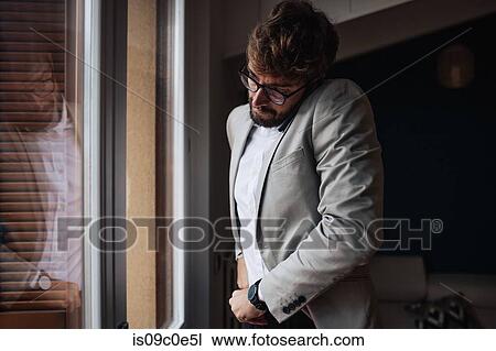 Stock Image - Mid adult man struggling to make smartphone call while tucking his shirt in. Fotosearch