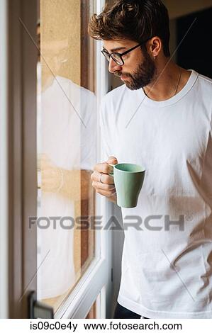 Mid adult man with coffee looking out through apartment window View Large Photo Image Stock Photo - Mid adult man with coffee looking out through apartment window. Fotosearch