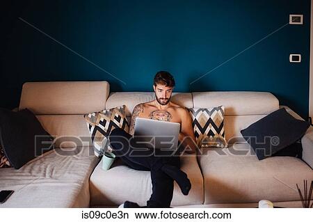 Mid adult man with tattooed chest on sofa using laptop View Large Photo Image Picture - Mid adult man with tattooed chest on sofa using laptop. Fotosearch