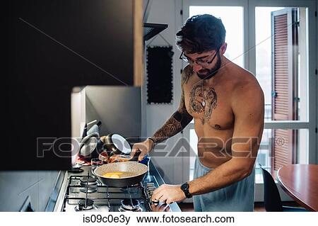 Stock Photo - Mid adult man with tattooed chest using gas hob. Fotosearch