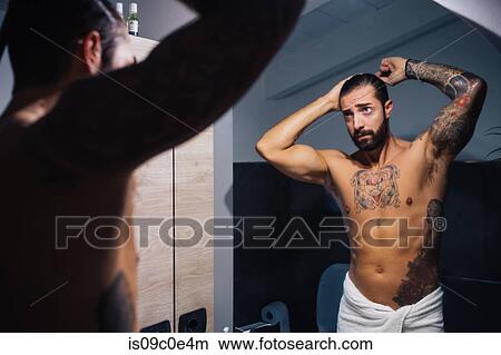 Picture - Mid adult man with tattoos combing hair at bathroom mirror, mirror image. Fotosearch
