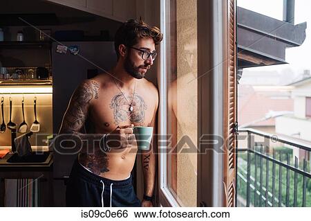 Mid adult man with tattoos looking out through kitchen window View Large Photo Image Stock Photograph - Mid adult man with tattoos looking out through kitchen window. Fotosearch