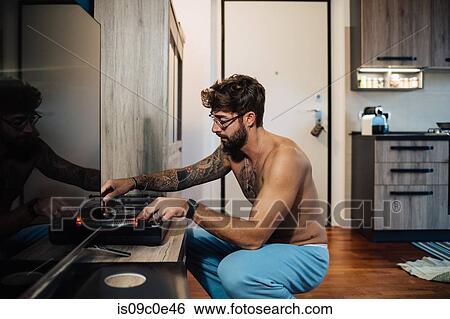 Stock Photograph - Mid adult man with tattoos playing vinyl on turntable. Fotosearch