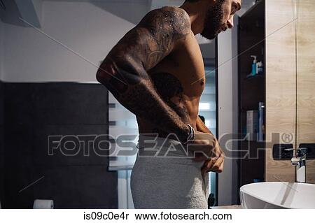 Mid adult man with tattoos putting towel around waist at bathroom mirror View Large Photo Image Stock Photography - Mid adult man with tattoos putting towel around waist at bathroom mirror. Fotosearch