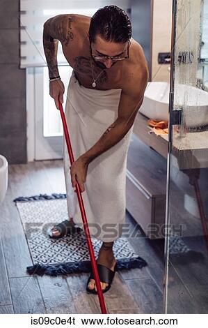 Stock Photograph - Mid adult man wrapped in towel cleaning bathroom floor. Fotosearch