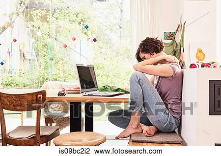 Stock Image - Mid adult woman at home, using laptop, worried expression. Fotosearch