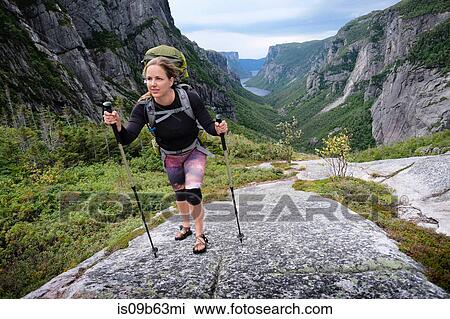 Stock Image - Mid adult woman hiking up rocky valley, Gros Morne National Park, Newfoundland, Canada. Fotosearch
