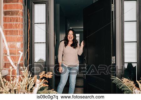 Stock Photography - Mid adult woman opening house front door, portrait. Fotosearch