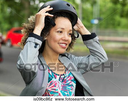 Stock Photo - Mid adult woman putting on bicycle safety helmet. Fotosearch