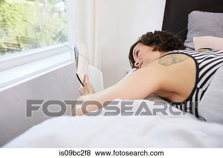 Mid adult woman, relaxing on bed, reading book View Large Photo Image Stock Photo - Mid adult woman, relaxing on bed, reading book. Fotosearch