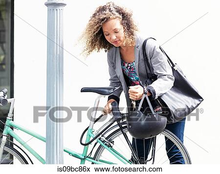 Stock Photo - Mid adult woman securing bicycle after journey. Fotosearch