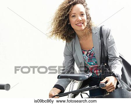 Stock Photo - Mid adult woman securing bicycle after journey. Fotosearch