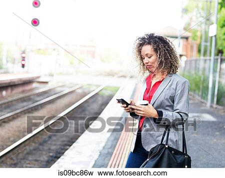 Mid adult woman standing on train platform, using smartphone, holding disposable coffee cup View Large Photo Image Stock Photo - Mid adult woman standing on train platform, using smartphone, holding disposable coffee cup. Fotosearch
