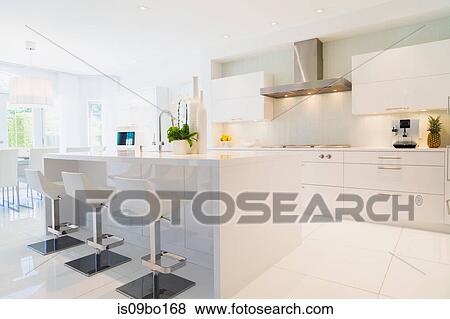 Modern kitchen with white Italian lacquered kitchen island and chrome barstools inside luxury residential home View Large Photo Image Stock Photo - Modern kitchen with white Italian lacquered kitchen island and chrome barstools inside luxury residential home. Fotosearch