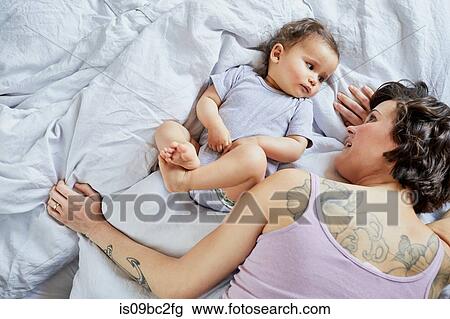 Stock Image - Mother and baby girl, lying on bed together. Fotosearch