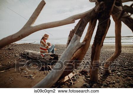 Stock Image - Mother and baby resting on fallen tree trunk on beach. Fotosearch