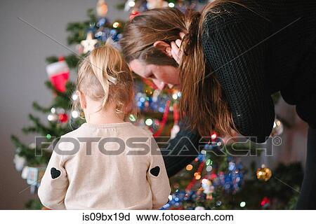 Stock Image - Mother and daughter decorating Christmas tree. Fotosearch