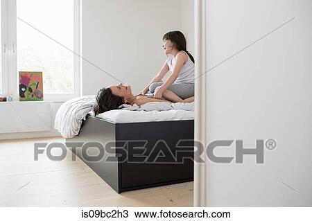 Mother and daughter fooling around in bedroom, daughter sitting on mother's chest View Large Photo Image Stock Image - Mother and daughter fooling around in bedroom, daughter sitting on mother's chest. Fotosearch