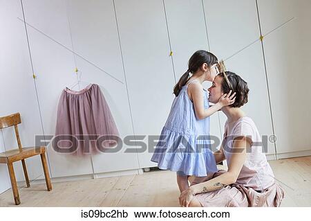 Stock Image - Mother and daughter in bedroom, face to face, daughter kissing mother on head. Fotosearch
